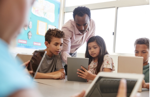 Teacher helping two elementary school students on a tablet