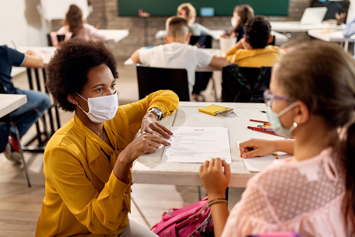 Teacher kneeling besides a student's desk assisting with school work