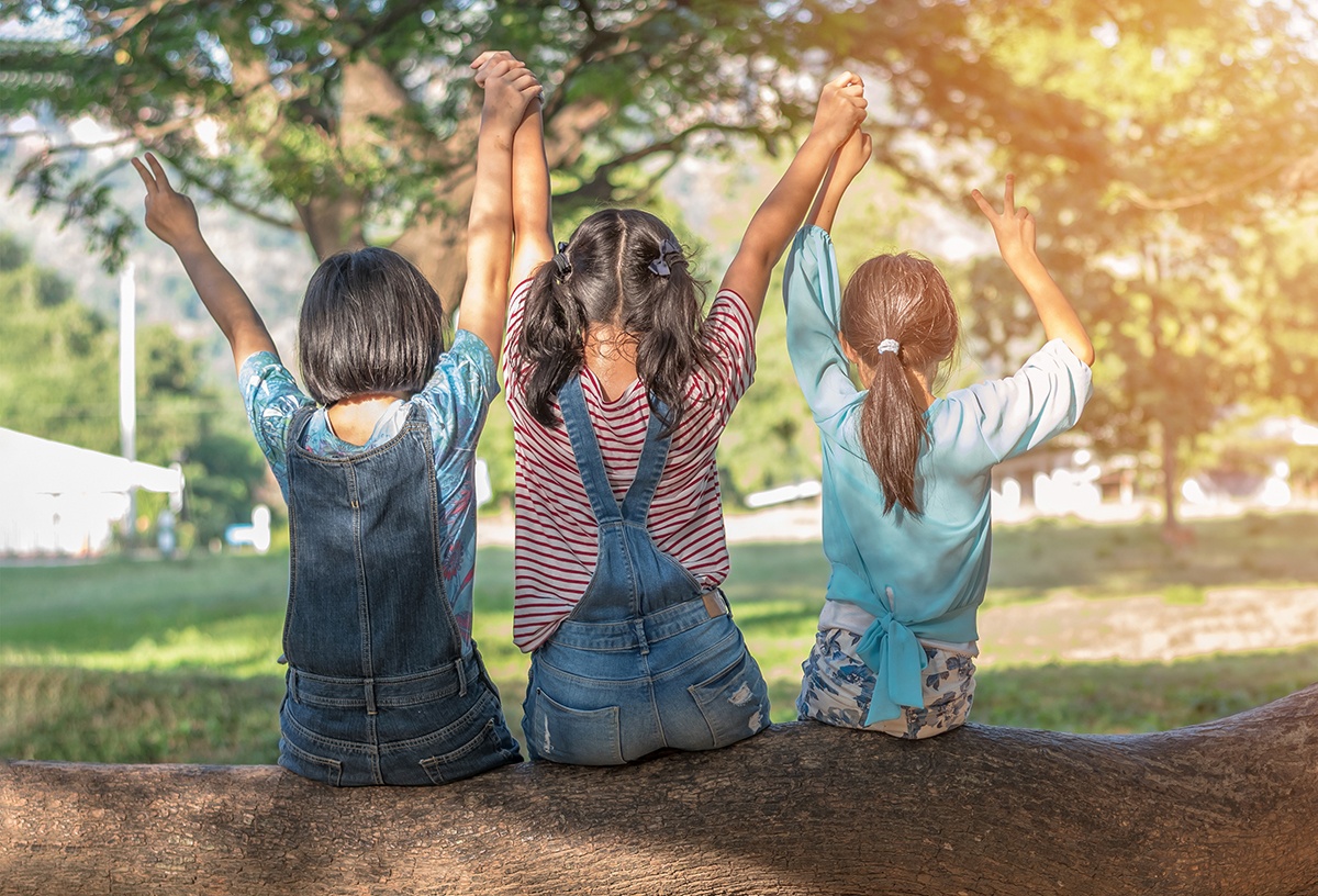 three girls sitting on a log holding their raised hands