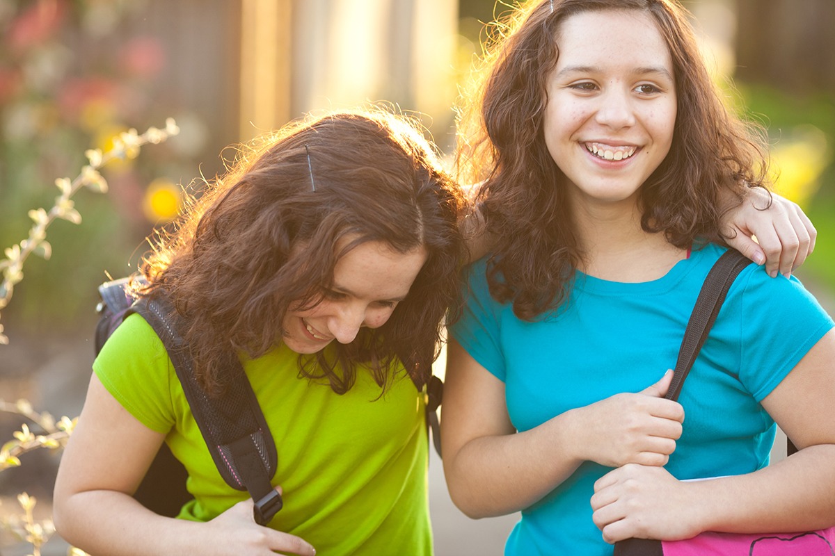 Two smiling girls walking with bags