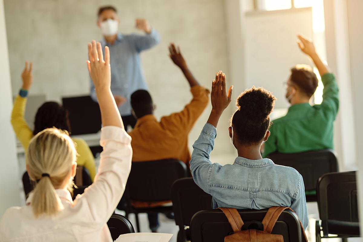 Students in a classroom all raising their hands to answer a question