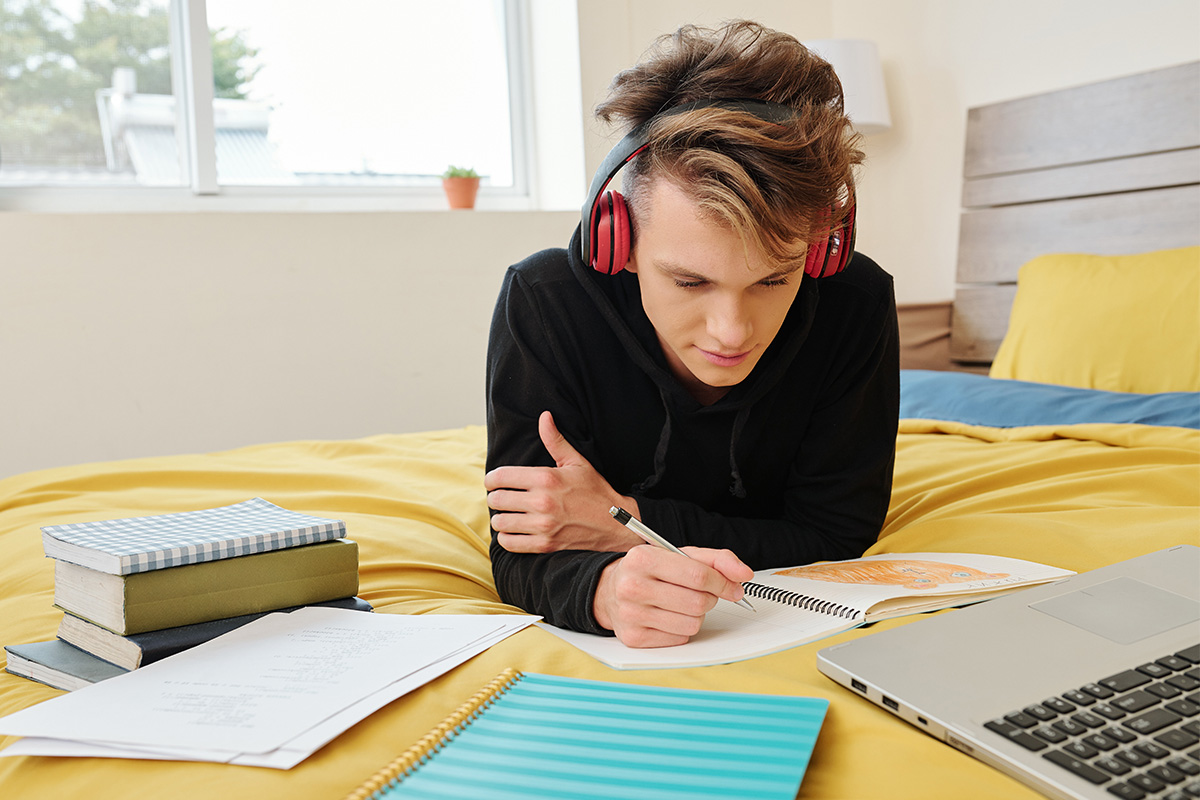 High schooler studies on their bed with headphones