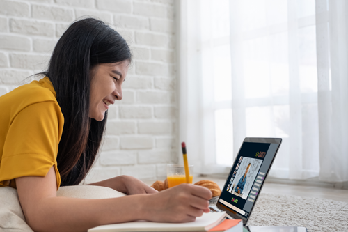 Middle school student writing in notebook and smiling at laptop