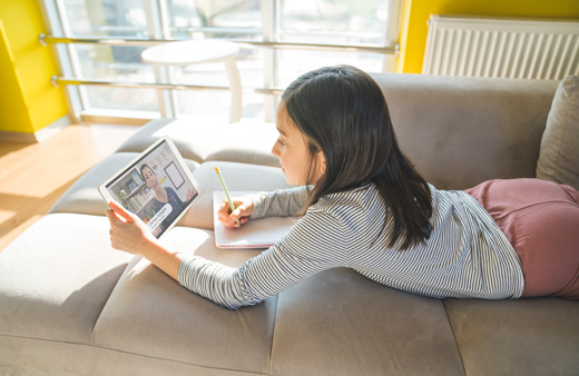 Elementary student watching teacher on tablet and writing on paper