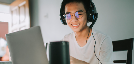 Student with headphones smiling in front of a laptop