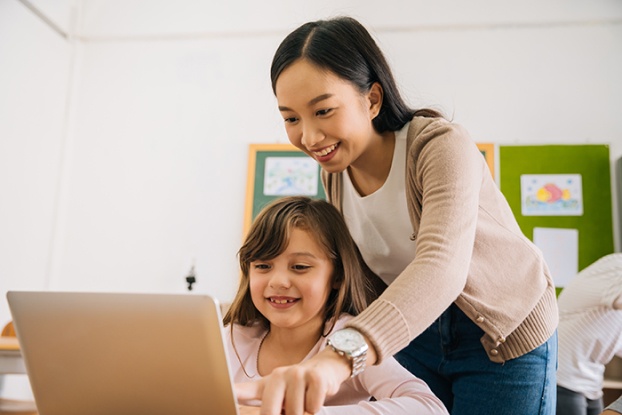 Elementary student and teacher looking at laptop together