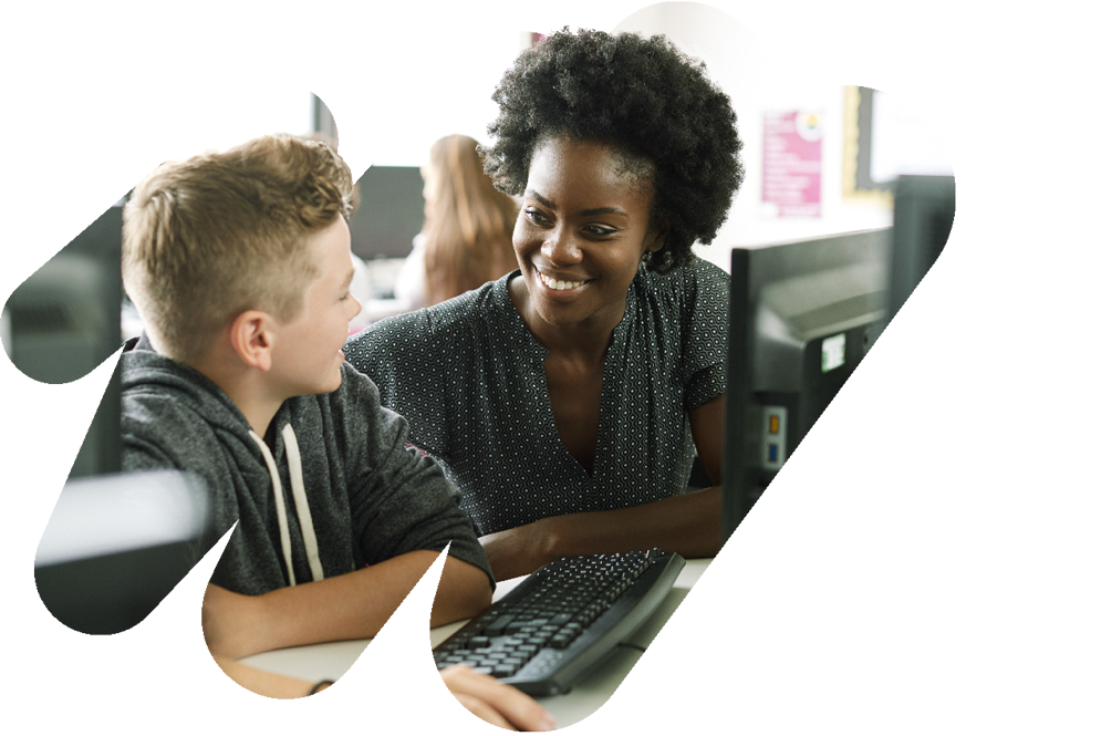 Teacher smiling at middle school student in front of a desktop computer