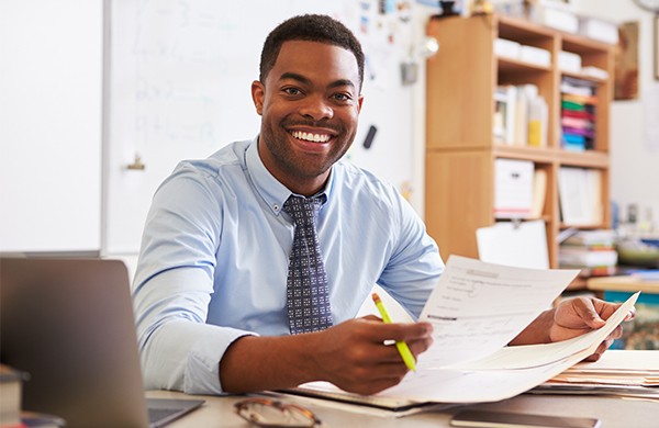 Smiling educator holding papers while sitting at a desk