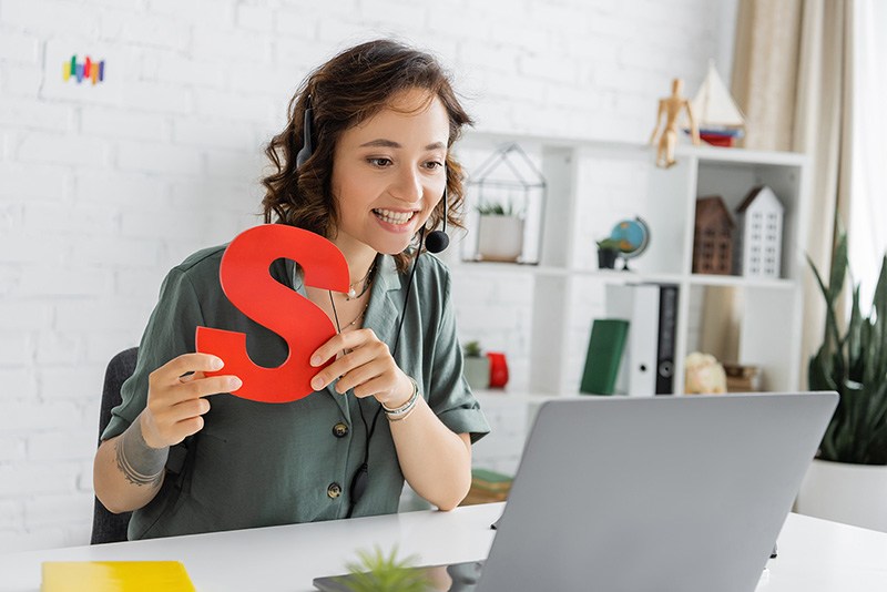 Speech teletherapist holding the letter S in front of a laptop