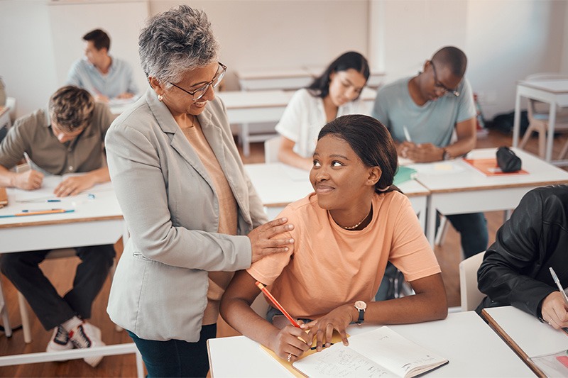 Uncertain-looking high school teacher looking over their shoulder at their encouraging teacher