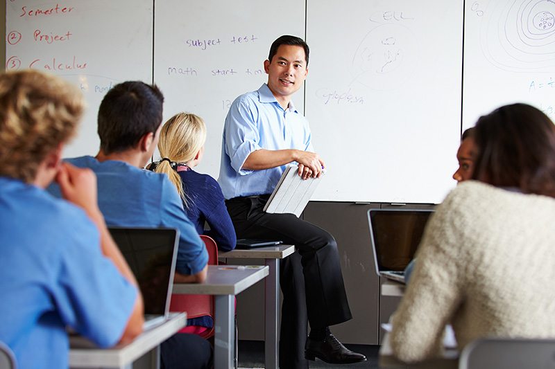 Teacher sitting and talking in front of a high school classroom