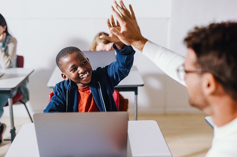 Elementary student working on laptop and high-fiving their teacher