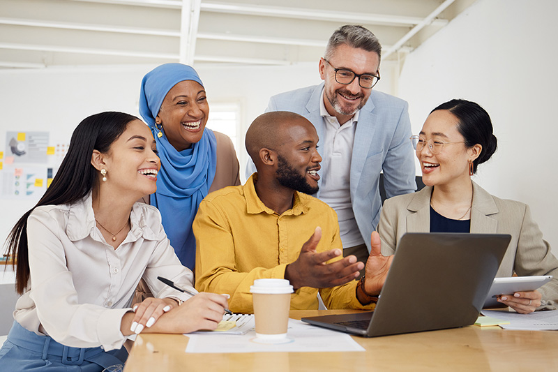 Group of five educators gathered around a laptop on a table and engaged in discussion