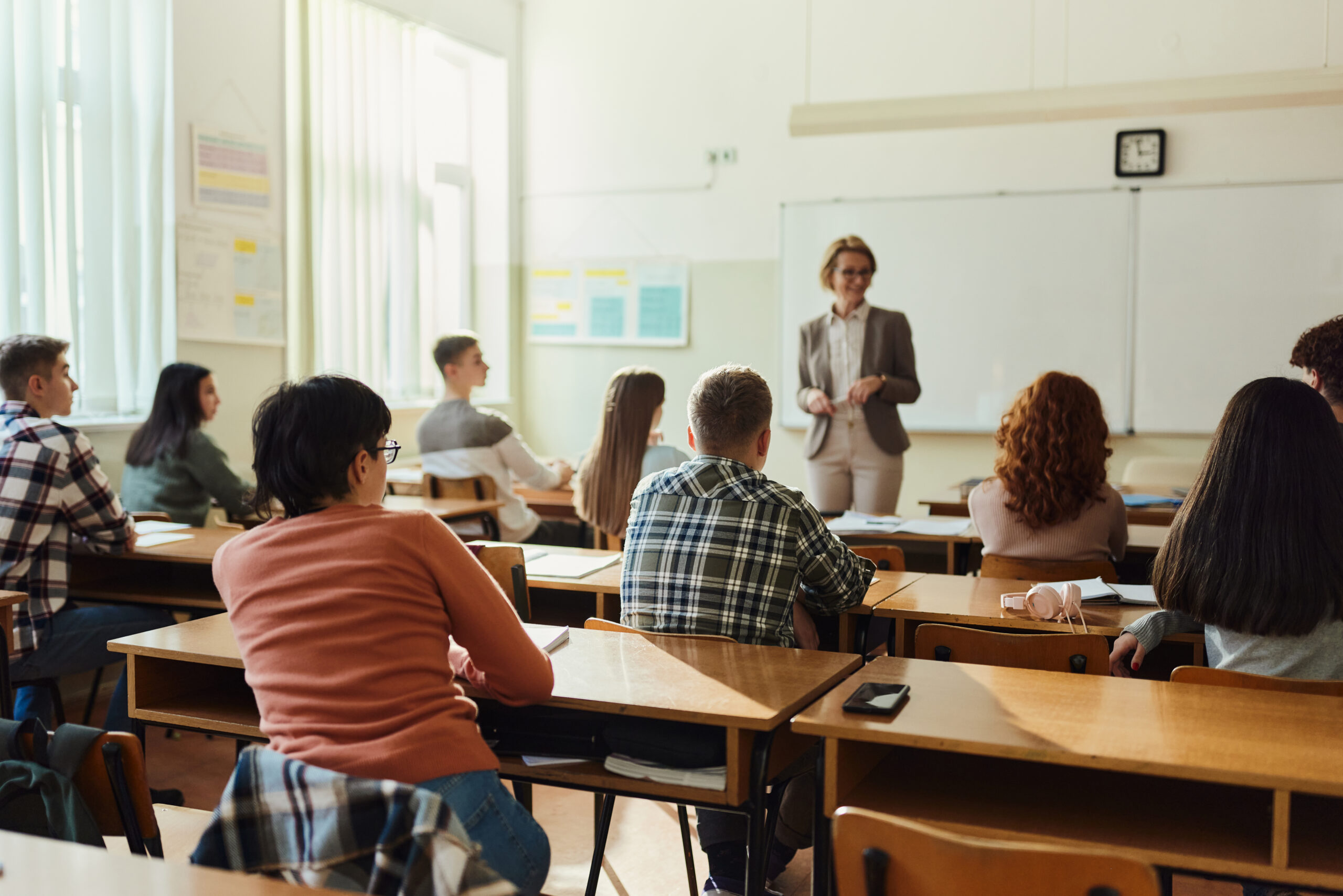 Rear view of large group of students listening to their teacher 