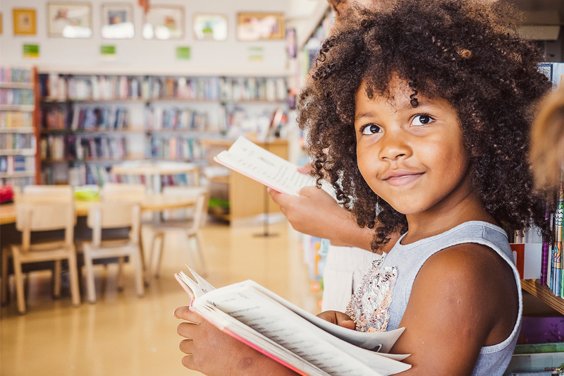 Elementary school children in a library leaning against a wall of books and reading
