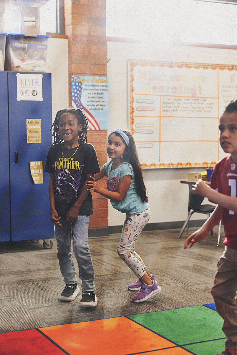 Two students stand side by side in a classroom, smiling during an activity.