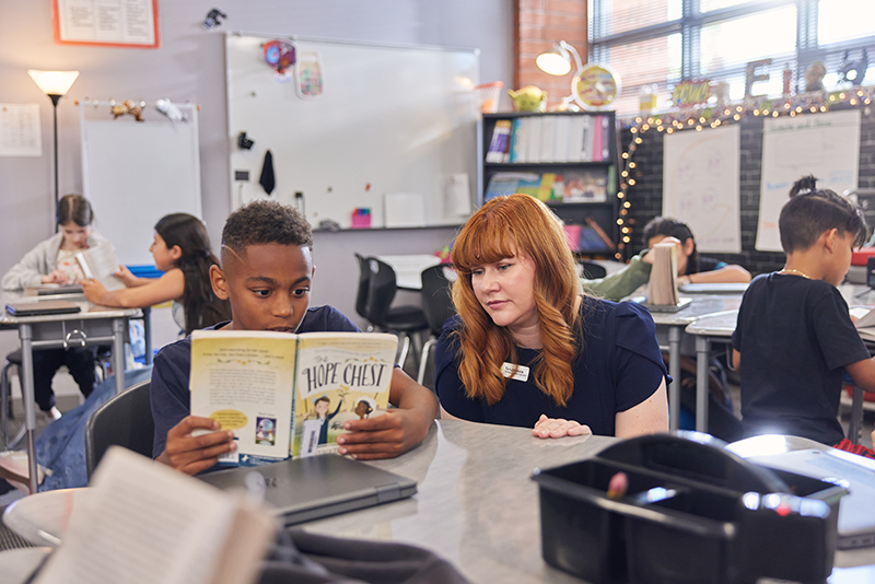 A student and a teacher read a book together.
