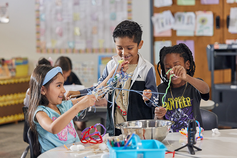 A group of first grade students build birds' nests out of colorful craft supplies.