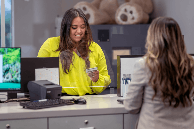 a smiling bank teller is assisting her customer