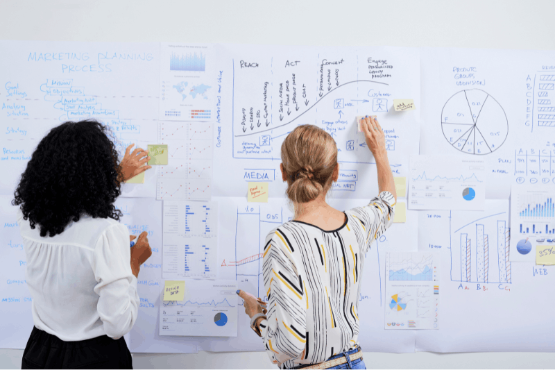 two people standing in front a board looking at marketing materials 