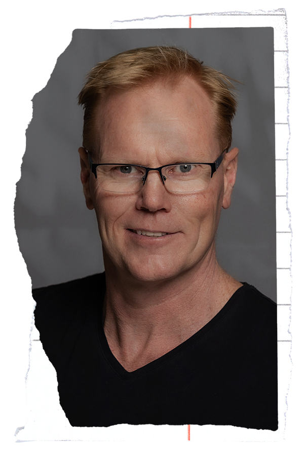 A strawberry blonde male with glasses in a black v-neck
