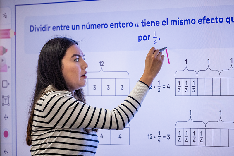 a teacher stands in front of a classroom board while writing on the board teaching her class