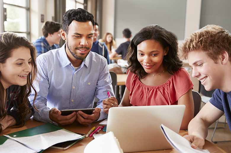 High school students looking at laptop with teacher